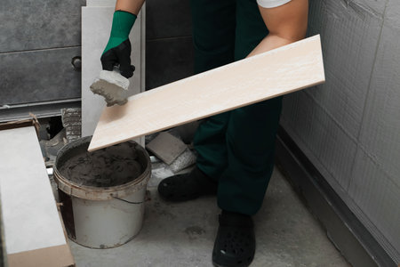 Worker applying adhesive mix on ceramic tile with spatula, closeup