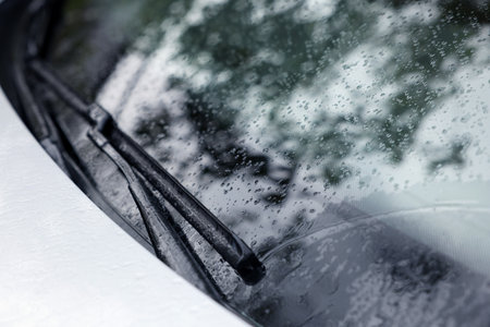 Wipers cleaning raindrops from car windshield outdoors