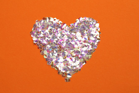 Heart made with shiny glitter on orange background, flat layの写真素材