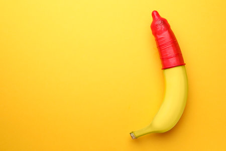 Banana with condom on orange background, top view and space for text. safe sex conceptの写真素材