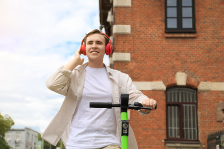 Handsome young man with headphones riding electric scooter on city streetの写真素材