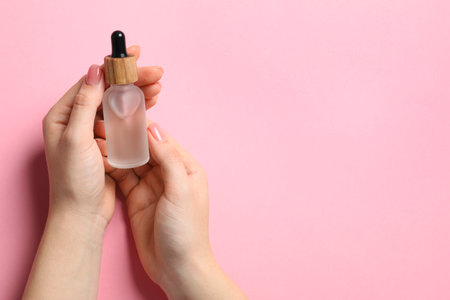 Woman holding bottle with serum on pink background, top view. Space for textの写真素材