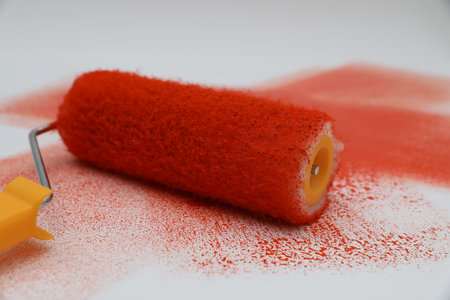 Roller brush and strokes of orange paint on white background, closeup