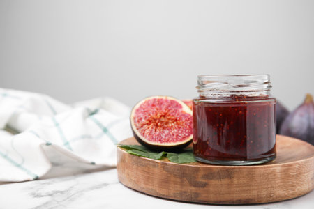 Glass jar of tasty sweet fig jam and fruits on white marble table. Space for textの写真素材