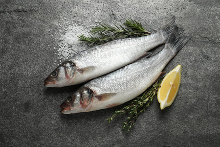 Tasty sea bass fish and spices on gray textured table, flat lay