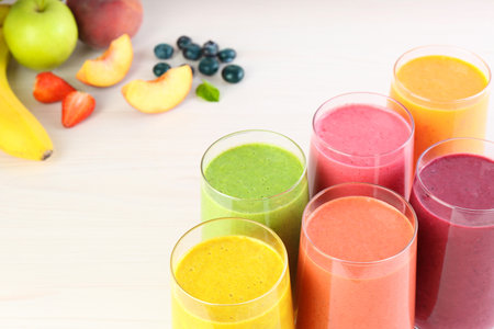 Fresh colorful fruit smoothies and ingredients on white wooden tableの写真素材