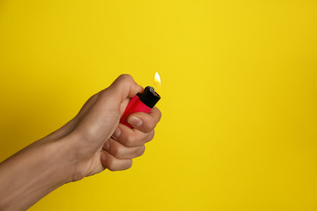 Woman holding pink lighter on yellow background, closeup. Space for textの写真素材