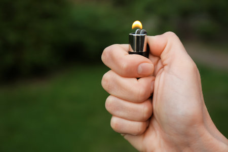 Man holding lighter with burning flame outdoors, closeup. Space for textの写真素材