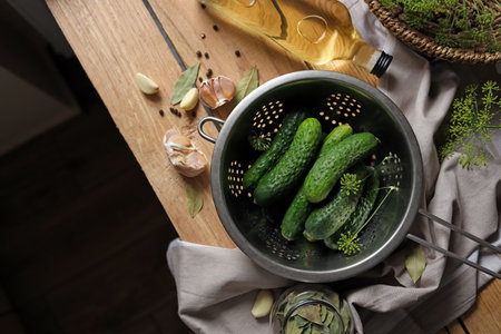Fresh cucumbers in colander and other ingredients prepared for canning on wooden table, flat lay. Space for textの写真素材