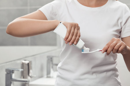 Woman applying toothpaste on brush in bathroom, closeupの写真素材