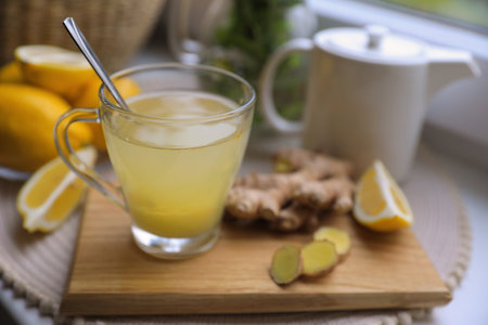 Glass of aromatic ginger tea and ingredients near window, space for text