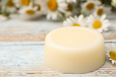 Solid shampoo bar and chamomiles on light wooden table, closeup. Space for textの写真素材