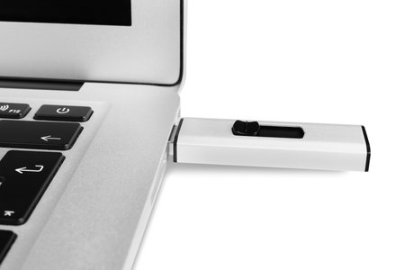 Modern usb flash drive attached to laptop on white background, closeup