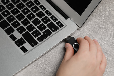 Woman attaching usb flash drive into laptop at gray table, closeup