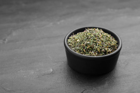 Bowl with dried thyme on black table, closeup. Space for text