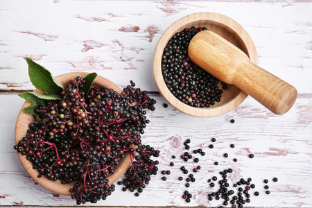 Tasty elderberries (Sambucus) on white wooden table, flat lay