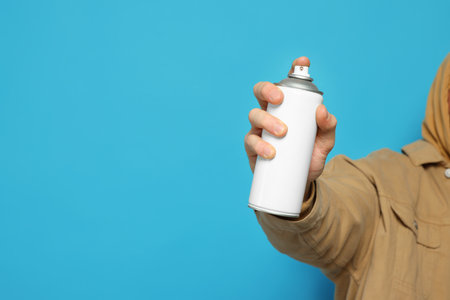 Man holding white can of spray paint on light blue background, closeup. Space for textの写真素材