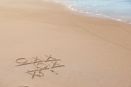 Tic tac toe game drawn on sand near sea, space for text