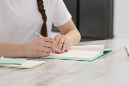 Woman writing in notebook at white marble table indoors, closeupの写真素材