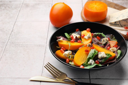 Delicious persimmon salad, knife and fork on tiled surface, space for textの写真素材