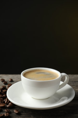 Cup of hot aromatic coffee and roasted beans on wooden table against dark backgroundの写真素材