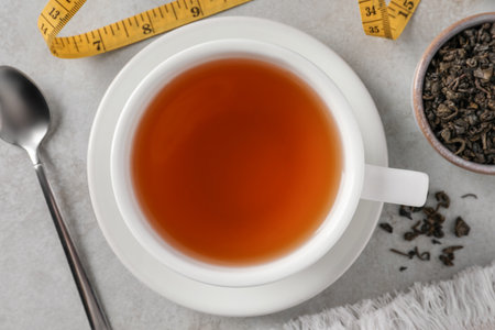 Cup of herbal diet tea and measuring tape on white table, flat lay. weight loss conceptの写真素材