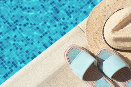 Stylish slippers and straw hat at poolside on sunny day, space for text. beach accessoriesの写真素材