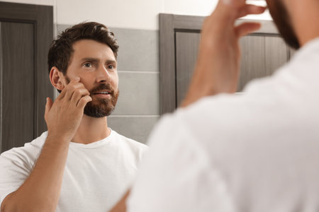 Handsome man applying cream on face in bathroomの写真素材