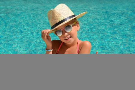 Cute little girl with glass of juice in swimming pool on sunny day
