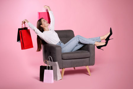 Happy young woman with shopping bags on armchair against light pink background. big saleの写真素材