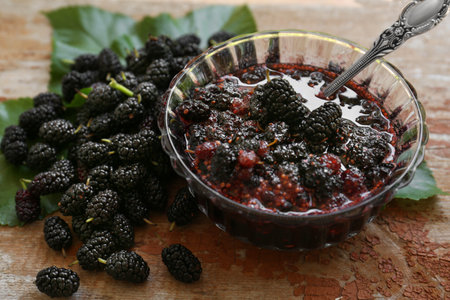 Delicious ripe black mulberries and bowl of sweet jam on wooden tableの写真素材