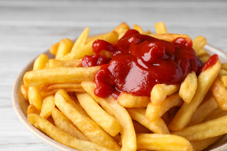 Bowl of tasty french fries on white wooden table, closeup
