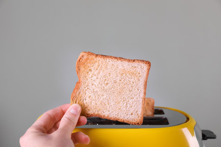 Woman taking off roasted bread from toaster against gray background, closeupの写真素材