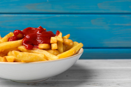 Bowl of tasty french fries on white wooden table, space for text