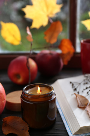 Beautiful burning candle and book on wooden table near window. autumn atmosphereの写真素材