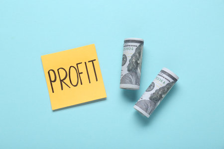 Sticky note with word Profit and rolled banknotes on turquoise background, flat layの写真素材