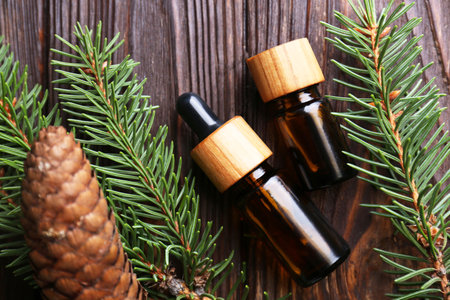 Bottles of aromatic essential oil, pine branches and cone on wooden table, flat layの写真素材