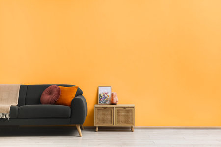 Stylish gray sofa with colorful pillows and wooden cabinet near pale orange wall indoors, space for text. interior designの写真素材
