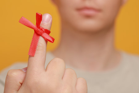 Man showing index finger with red tied bow as reminder against orange background, focus on hand