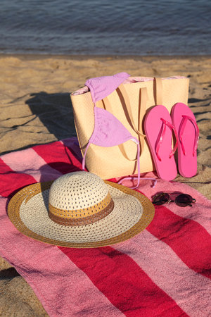 Towel with bag and beach accessories on sand near seaの写真素材