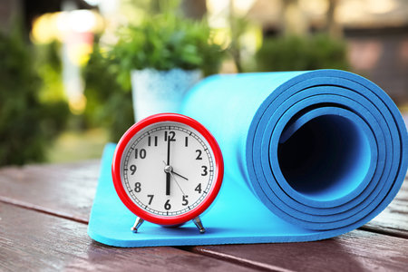 Alarm clock and fitness mat on wooden table outdoors. morning exerciseの写真素材