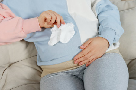 Pregnant woman sitting on sofa with baby socks, closeupの写真素材