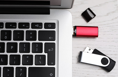 Modern usb flash drive attached to laptop on white wooden table, flat lay