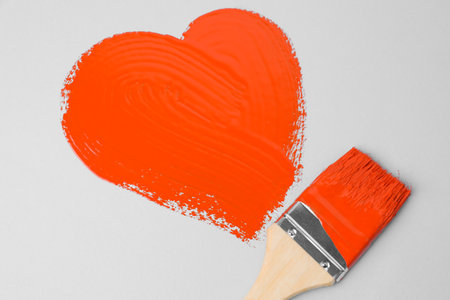 Heart shape made with orange paint and brush on white backgroundの写真素材