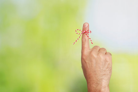 Man showing index finger with tied bow as reminder on green blurred background, closeup. Space for textの写真素材