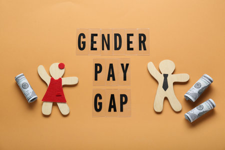 gender pay gap. Wooden figures of man and woman with dollar banknotes on pale orange background, flat layの写真素材