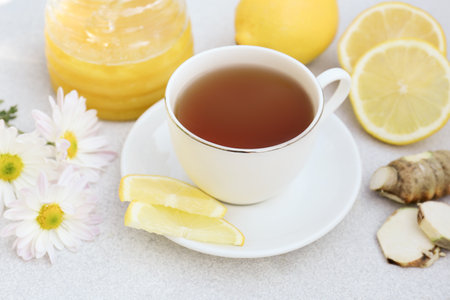Cup of delicious tea with honey, lemon and ginger on white tableの写真素材