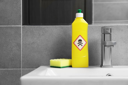 Bottle of toxic household chemical with warning sign and scouring sponge in bathroom, space for textの写真素材