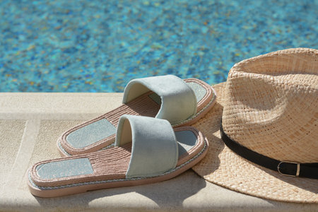 Stylish slippers and straw hat at poolside on sunny day. beach accessories