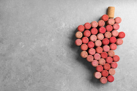 Grape made of wine bottle corks on gray table, top view. Space for text